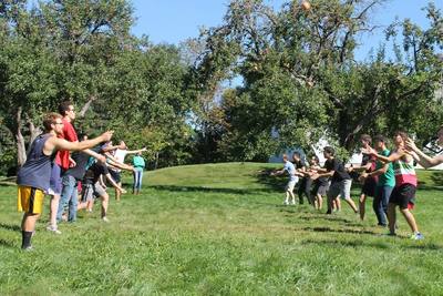 Glee Club members standing in two lines facing each other on a grassy lawn. The Glee Club members are throwing and catching items as a part of a game while on choir retreat. 