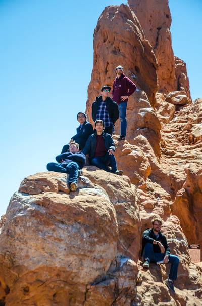 Three Glee Club members sitting and two standing on top of a large rock formation.