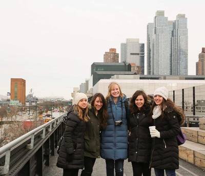 Five Radcliffe Choral Society members standing in a semi-circle with their arms around each other, posing for a picture on the New York Highline walk. 