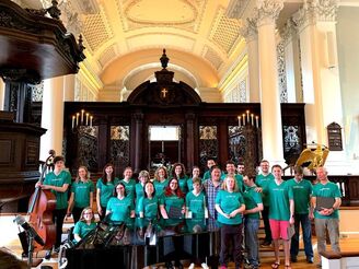 Cambridge Common Voices singers standing in front of Appleton Chapel inside the Harvard Memorial Church sanctuary. All are wearing green 