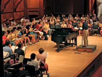 Harvard Summer Chorus singers rehearsing in rows on the Sanders Theatre stage