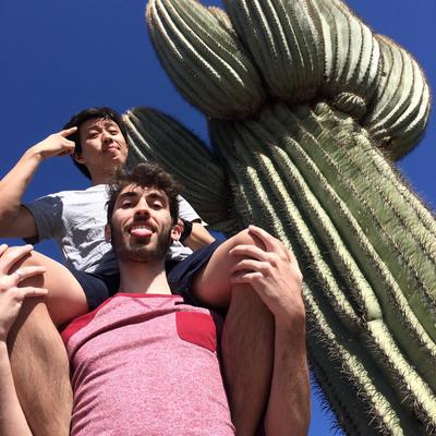 Two Glee Club members, one sitting on the others shoulders, standing in front of a large cactus. 